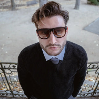 Homme portant des lunettes de soleil de luxe Elyonel avec un pull noir et une cravate, look moderne et professionnel.